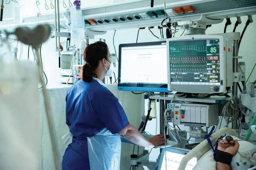 Hospital nurse monitoring a critically ill patient's vital signs using bedside monitoring equipment in an intensive care unit